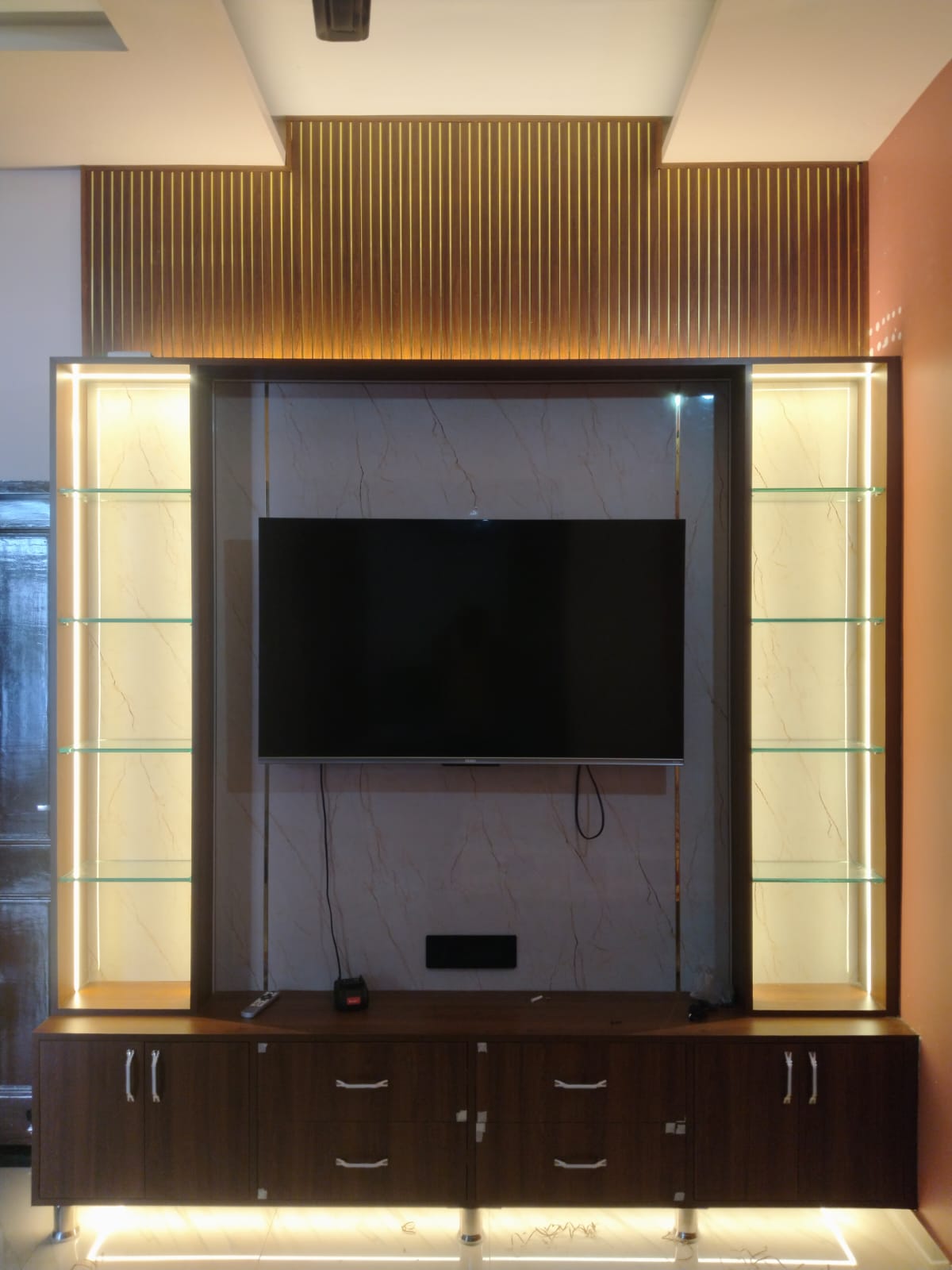 Illuminated TV wall unit with marble back panel, LED cove lighting, fluted top and lit glass display shelves